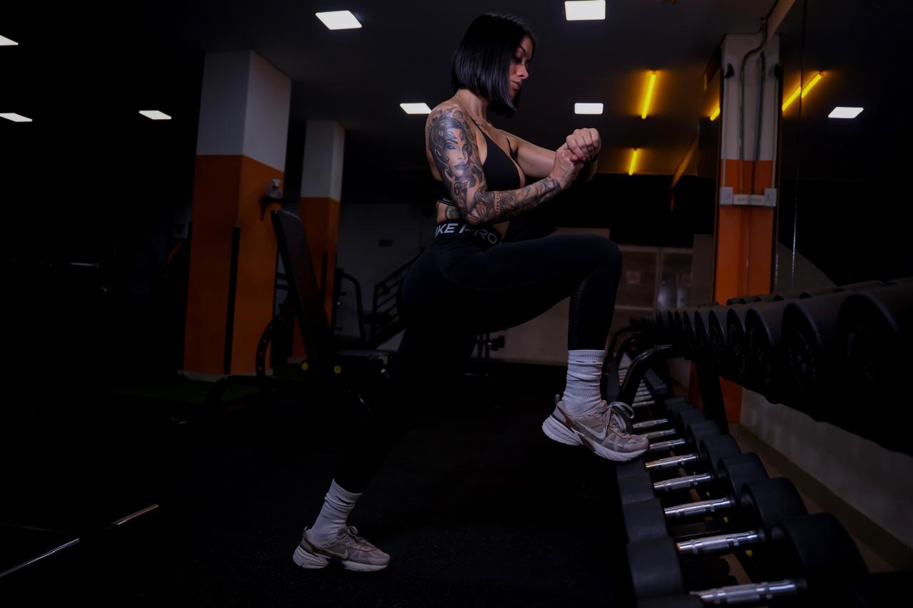 Alma mid-lunge at the dumbbell rack